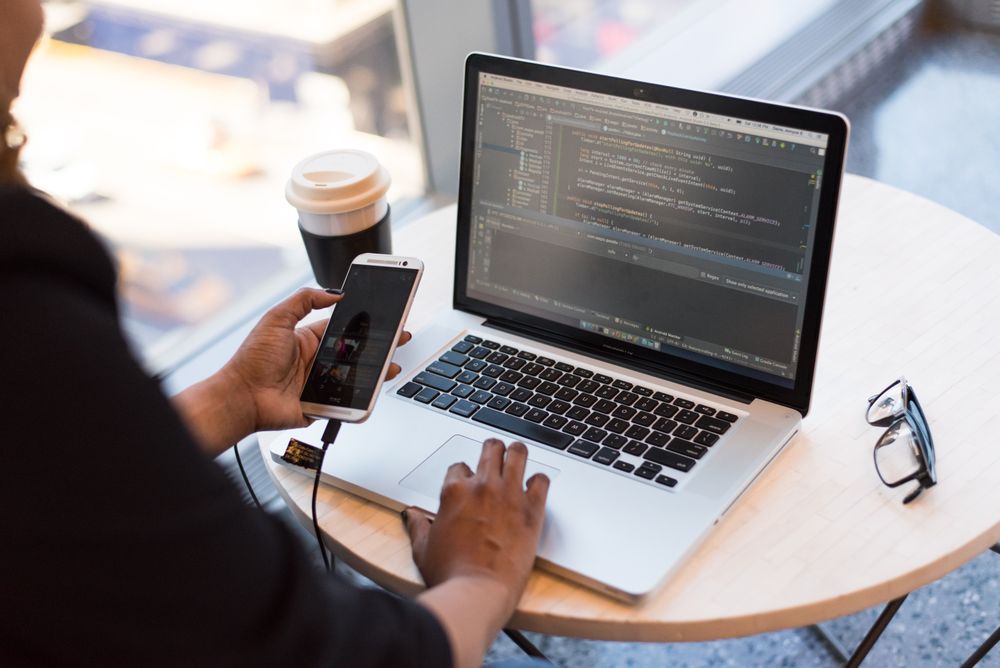 Pessoa em uma estação de trabalho usando notebook e monitor, vista de costas